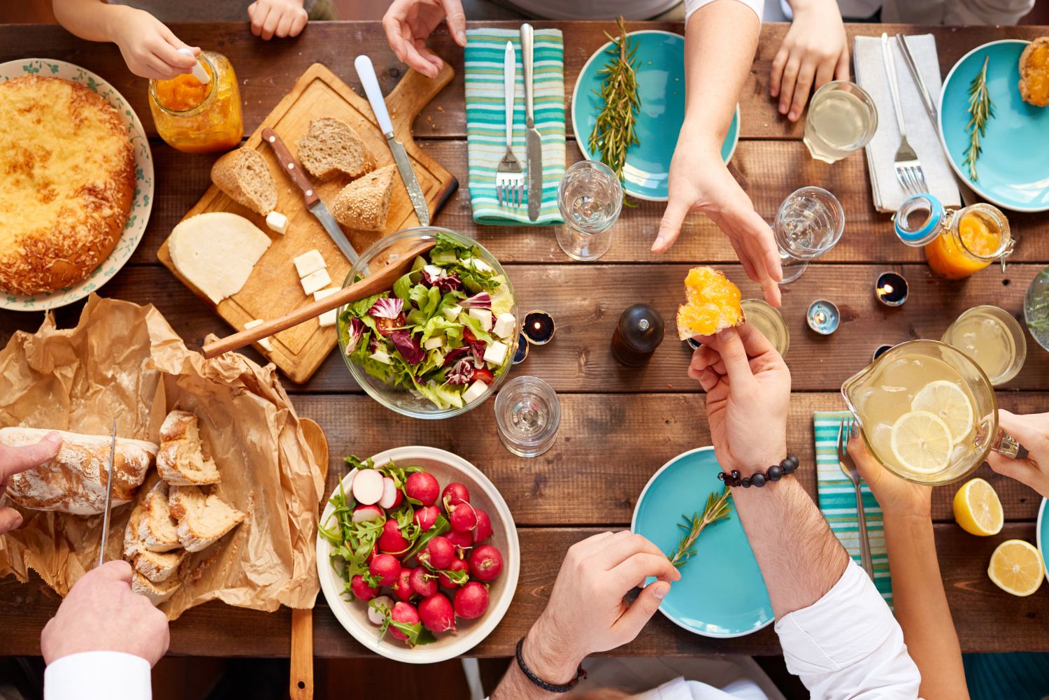 stół z jedzeniem; ręce osób sięgających po jedzenie;