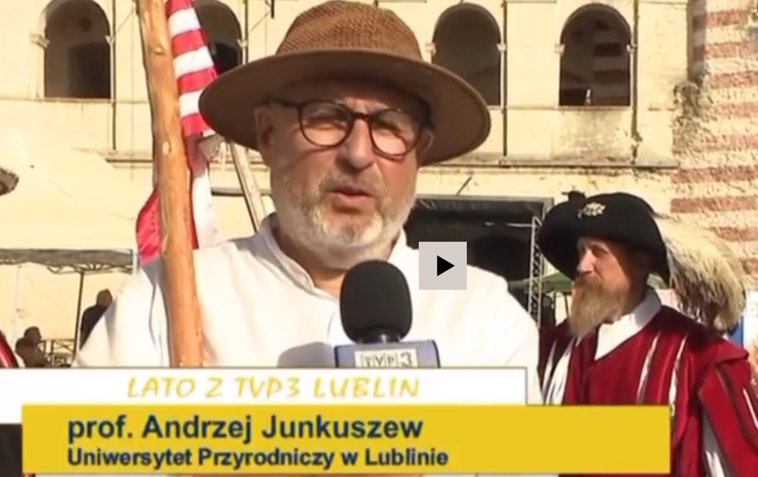 Prof. Andrzej Junkuszew w kapeluszu z kijem w tle Zamek w Janowcy, wypowiedź dla telewizji