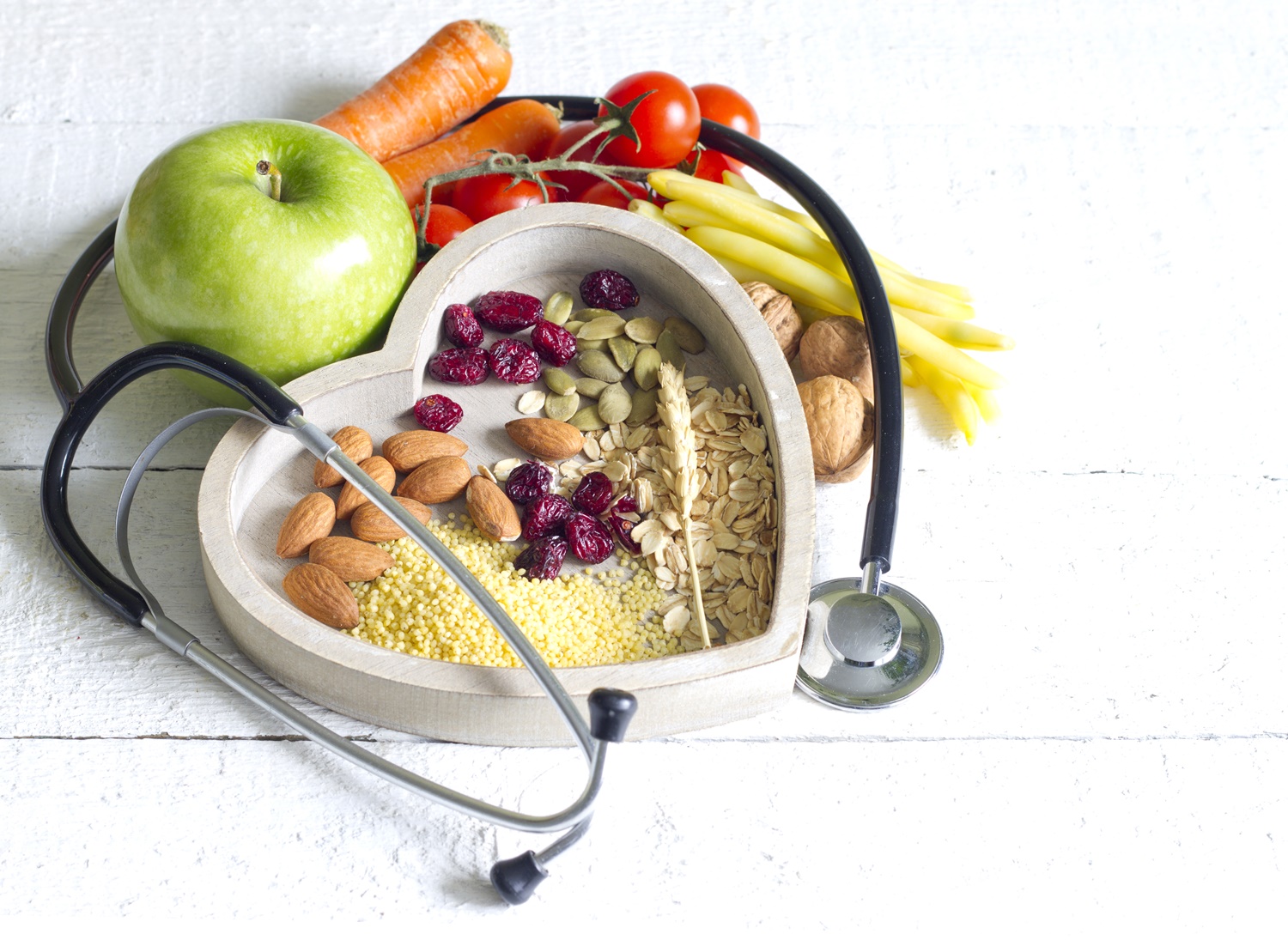 ziarna w naczyniu o kształcie serca, warzywa, jabłko i stetoskop dookoła