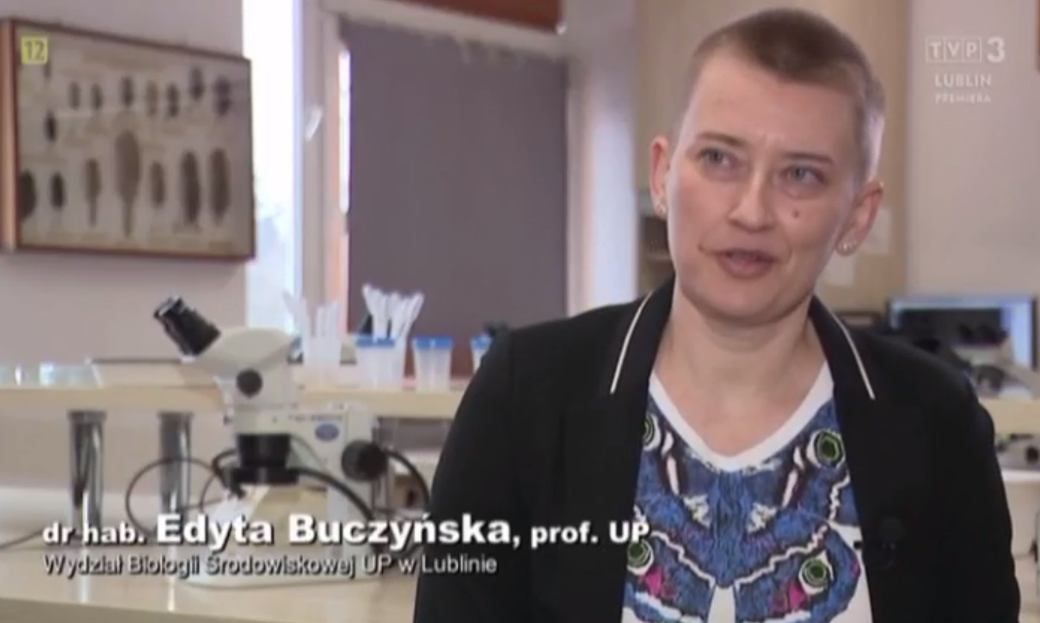 dr. hab. Edyta Buczyńska, prof. uczelni - krótkie blond włosy, czarny żakiet, koszulka z niebieskim motylem, w tle pracownia biologiczna