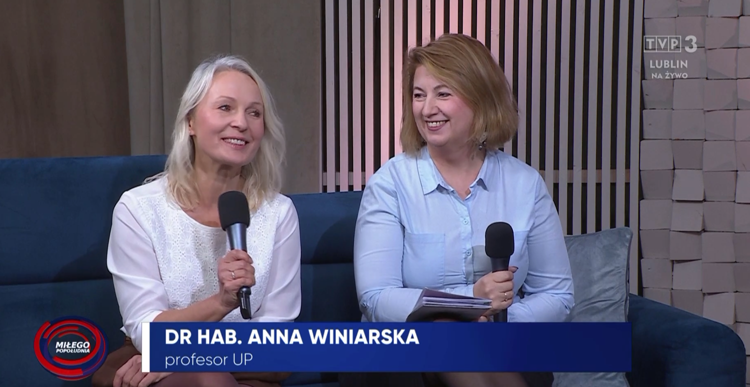 prof. Anna Winiarczyk w białej bluzce, siedzi, trzyma mikrofon obok pani w niebieskiej bluzce