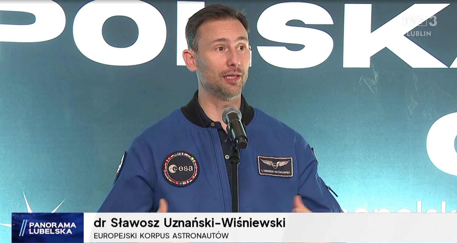 dr Sławosz Uznański-Wiśniewski przy mikrofonie w kurtce ze stacji ISS, w tle napis Polska