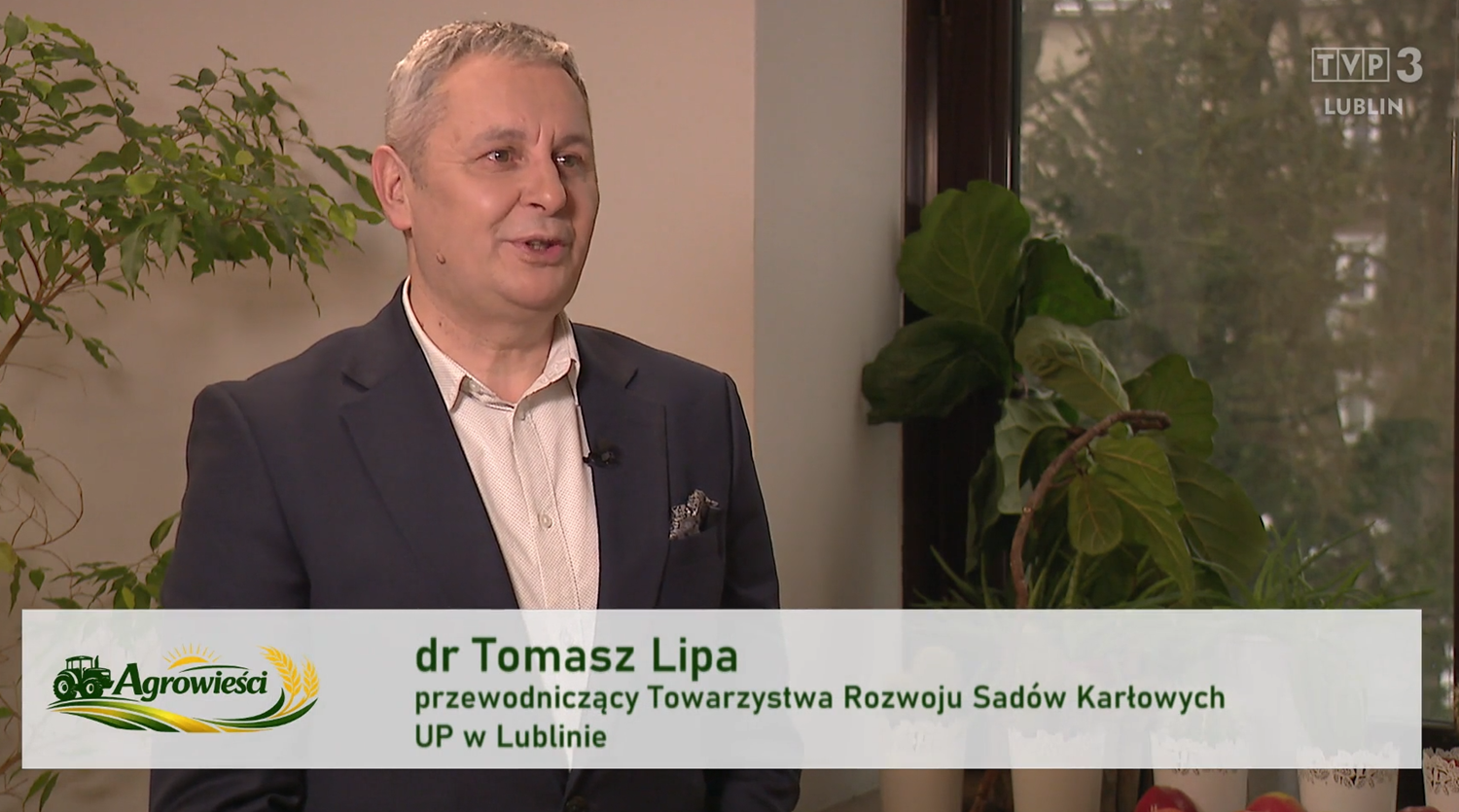 dr Tomasz Lipa w szarym garniturze, na tle roślin, z przodu pasek z jego nazwiskiem i funkcjami oraz logo Programu
