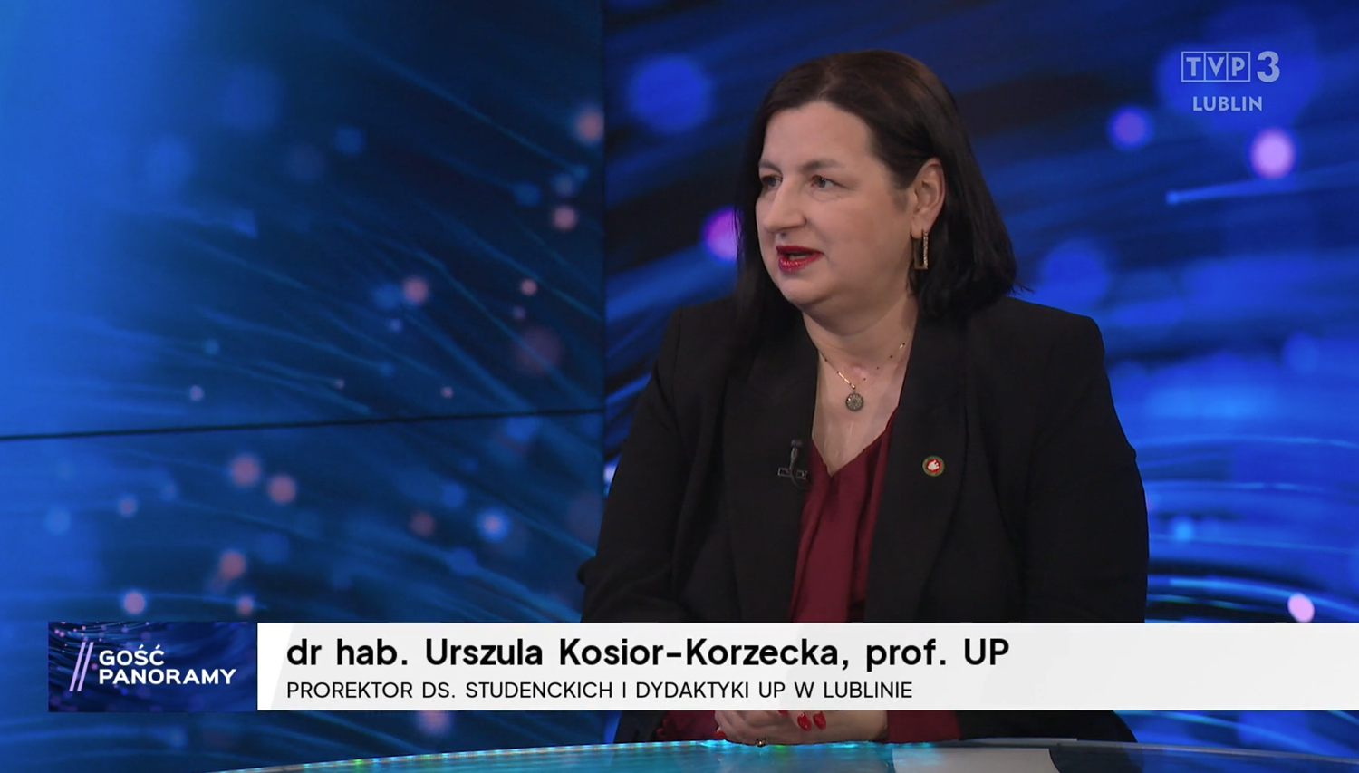 Prorektor Urszula Kosior-Korzecka w&nbsp;czarnym żakiecie, bordowej bluzce, siedzi na niebieskim tle