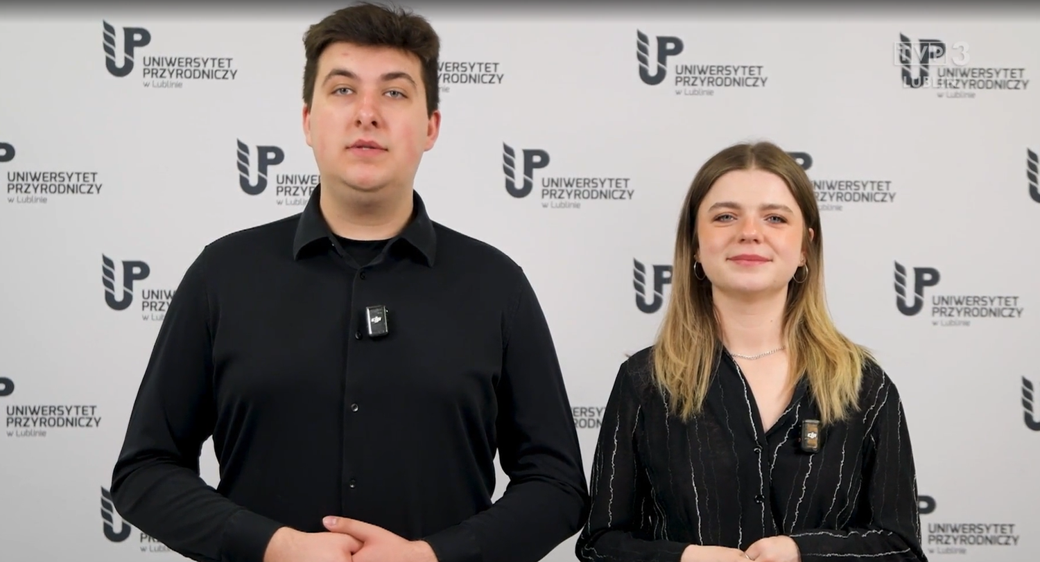 student i&nbsp;studentka ubrani na czarno stoi na tle białej ścianki z&nbsp;czarnym logo Uniwersytetu Przyrodniczego w&nbsp;Lublinie