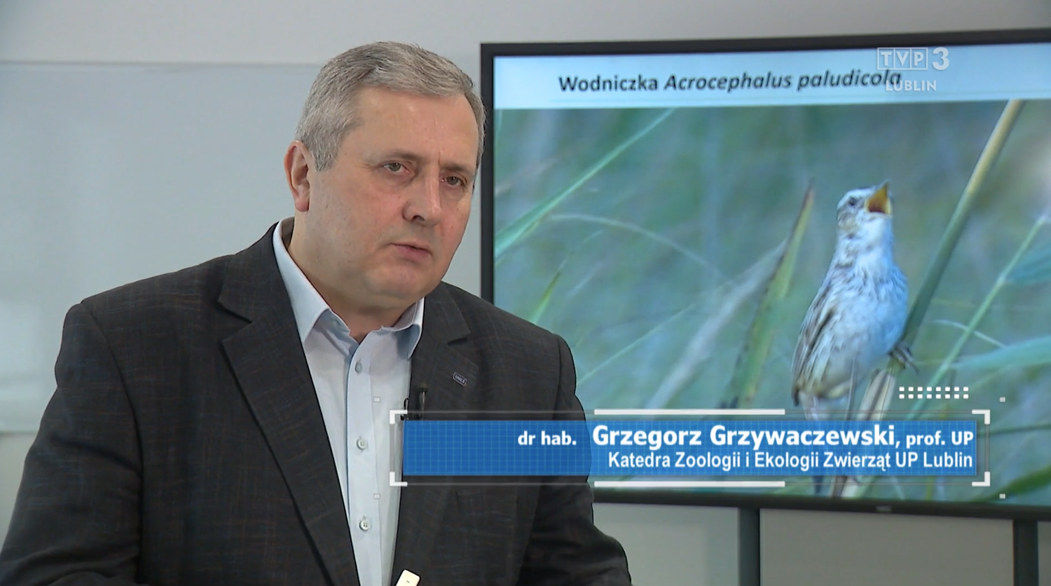 prof. Grzegorz Grzywaczewski w&nbsp;szarej marynarce, jasnoniebieskiej koszuli, na dole - na niebieskim tle - biały napis z&nbsp;jego nazwiskiem i&nbsp;miejscem pracy- w&nbsp;tle slajd w&nbsp;szarozielonych barwach z&nbsp;ptakiem-wodniczką