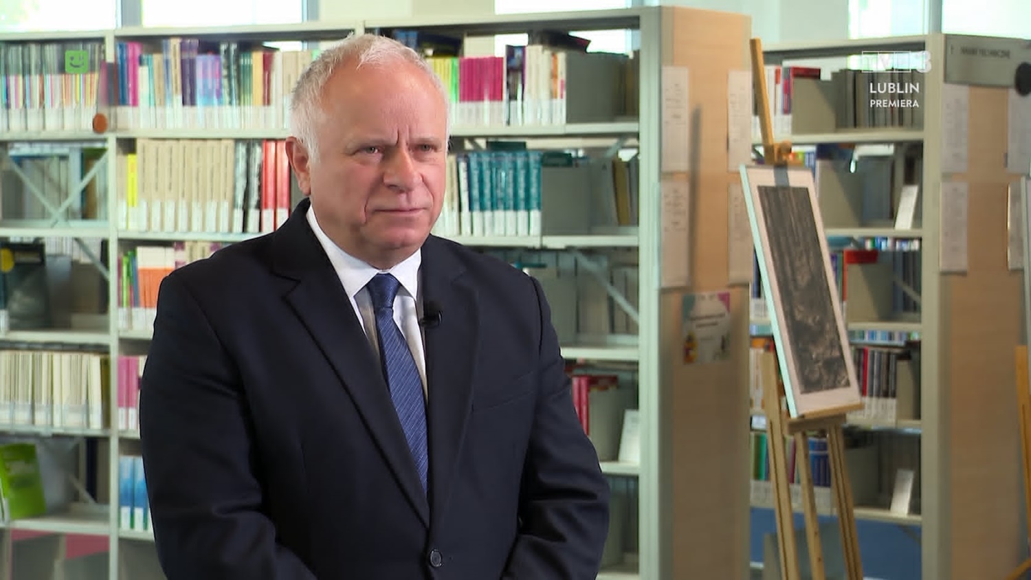 Rektor prof. dr hab. Krzysztof Kowalczyk w czarnym garniturze, niebieskim krawacie, w tle- półki z książkami